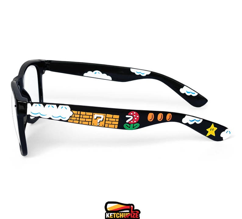 Picture of black prescription glasses, hand-painted with a Super Mario 8 bit video game inspired design. Including 1up mushrooms, Piranha plant, Question blocks, Starman and Brick Blocks on a black background.