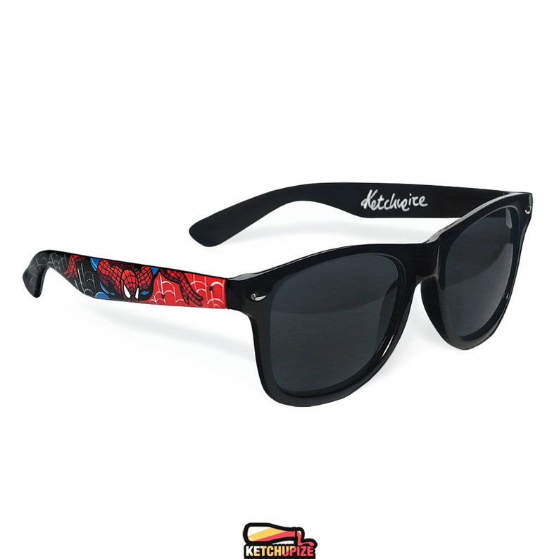 Picture of black sunglasses, hand-painted with a Spiderman comic theme design, showing Spiderman against spider web and the city skyline, in red, blue and black colors.