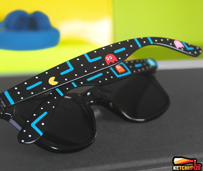 Picture of black sunglasses, hand-painted with an Arcade video game inspired design, including yellow, red, pink, orange and blue monsters and ghosts, white dots and blue lines.