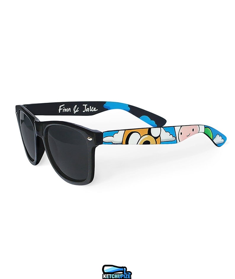 Picture of black sunglasses, hand-painted with an Adventure Time inspired design, including Finn the human and Jake the dog on a blue background with white clouds, in white, blue and yellow colors.