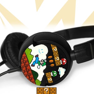 Picture of black headphones, hand-painted with a Super Mario 8 bit video game inspired design. Including the Mario brothers, Mario and Luigi, 1up mushrooms, Piranha plant, Question blocks, Starman and Brick Blocks on a black background.