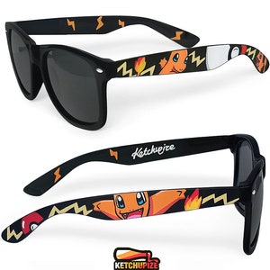 Picture of black sunglasses, hand-painted with a Pokémon design, including orange Charmander and red and white Pokeballs on a black background, in orange, yellow and red colors.