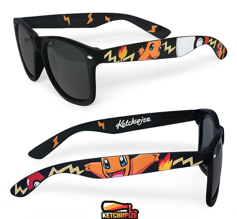 Picture of black sunglasses, hand-painted with a Pokémon design, including orange Charmander and red and white Pokeballs on a black background, in orange, yellow and red colors.