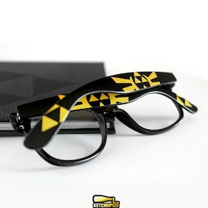 Picture of black clear lens glasses, hand-painted with a Legend of Zelda inspired design, including yellow triforce and wingcrest, in black and yellow colors.