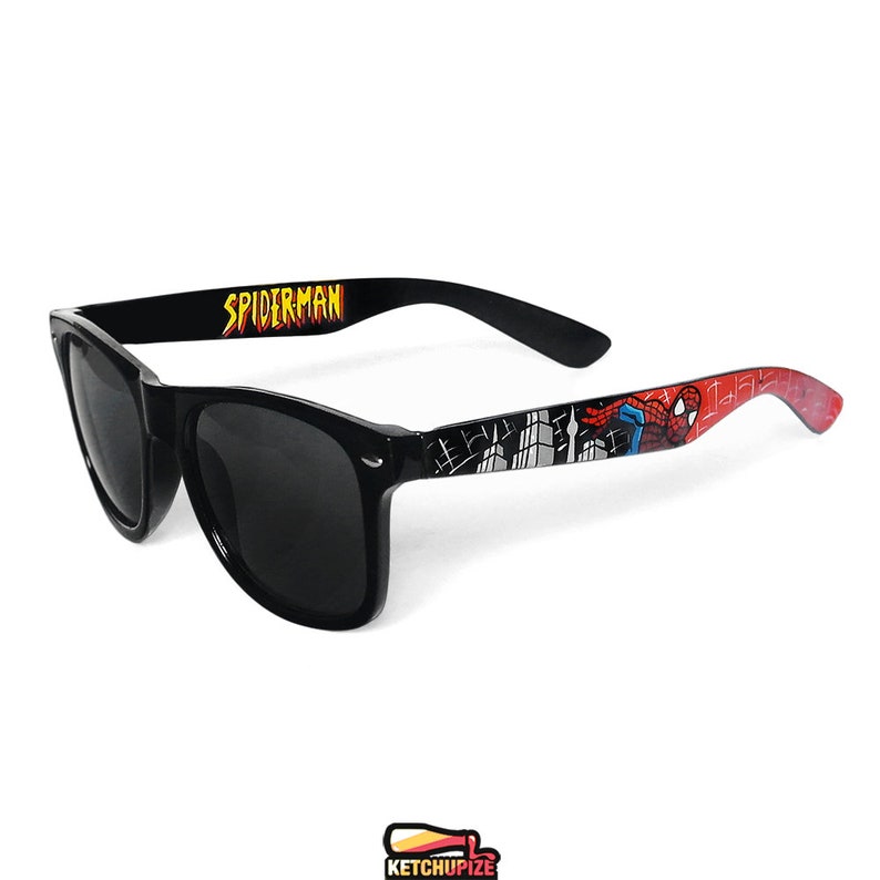 Picture of black sunglasses, hand-painted with a Spiderman comic theme design, showing Spiderman against spider web and the city skyline, in red, blue and black colors.