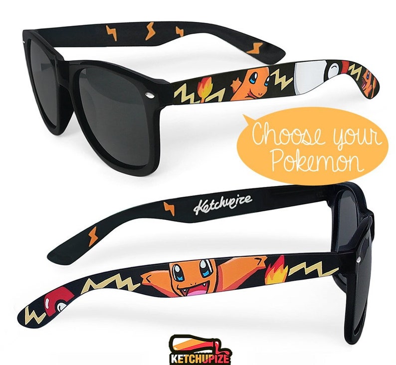 Picture of black sunglasses, hand-painted with a Pokémon design, including orange Charmander and red and white Pokeballs on a black background, in orange, yellow and red colors.