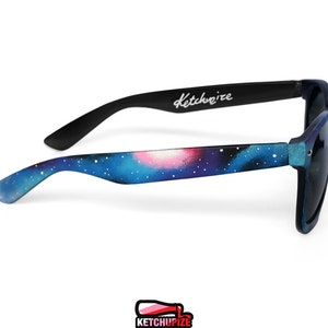 Picture of black sunglasses, hand-painted with a galaxy design in blue, purple and pink colors.