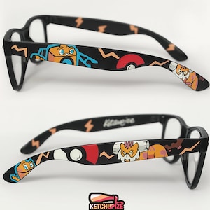 Picture of black clear lens glasses, hand-painted with a Pokémon design, including Landorus-Therian and Rotom-Wash and red and white Pokeballs on a black background, in orange, yellow, blue and red colors.