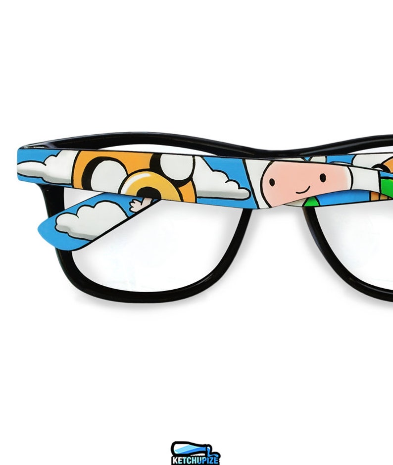 Picture of black clear lens glasses, hand-painted with an Adventure Time inspired design, including Finn the human and Jake the dog on a blue background with white clouds, in white, blue and yellow colors.