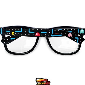 Picture of black prescription glasses, hand-painted with an Arcade video game inspired design, including yellow, red, pink, orange and blue monsters and ghosts, white dots and blue lines.