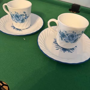 Könnte beinhalten: Eine weiße Keramik-Tasse mit schwarzem Henkel und dem Text "But First, Coffee" in fetter, schwarzer Schrift. Die Tasse steht vor einem verschwommenen Hintergrund, der eine gemütliche Umgebung suggeriert.