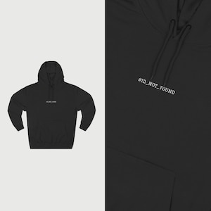 Puede incluir: Sudadera con capucha negra con cordón y bolsillo delantero. El texto "#ID_NOT_FOUND" está impreso en blanco en la parte superior derecha del pecho y en la parte delantera de la sudadera.