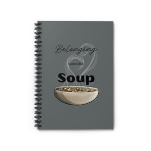 May include: Spiral-bound notebook with a gray cover featuring the words "Belonging tastes like Soup." The design includes an illustration of a bowl of soup with steam rising above it. The notebook's spiral binding is visible on the left side.