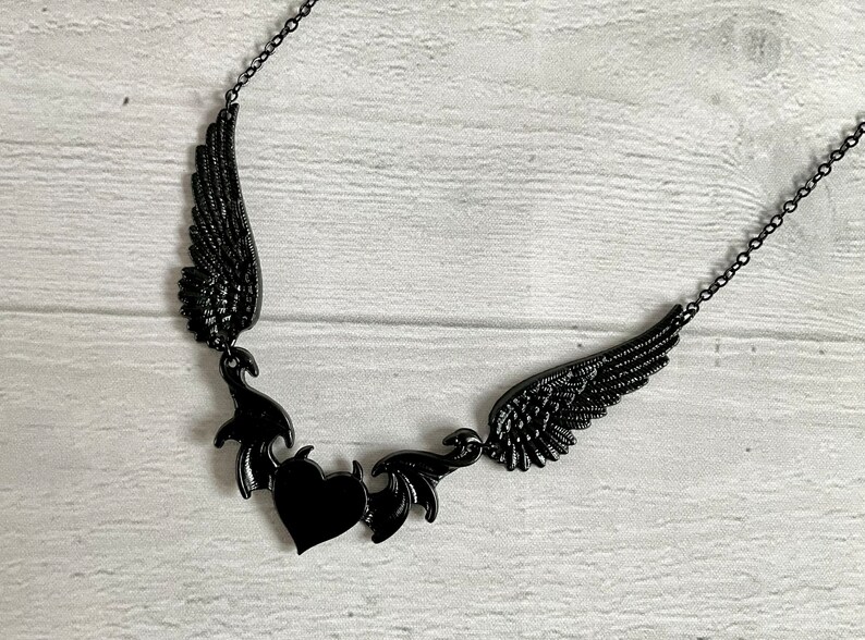 May include: Black necklace with a heart and two wings. The wings are made of metal and have a detailed design. The heart is also made of metal and has a black finish.
