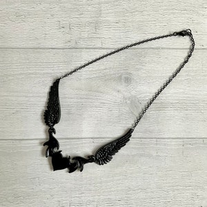 May include: A black necklace with a heart pendant and two wings on either side. The necklace is made of a delicate chain.