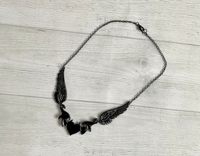 May include: A black necklace with a heart pendant and two wings on either side. The wings are detailed and intricate.