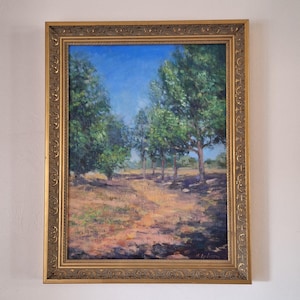 May include: An oil painting of a landscape scene featuring a path leading through a field of dry grass towards a line of trees. The trees have green foliage and are set against a bright blue sky. The painting is in a gold ornate frame.