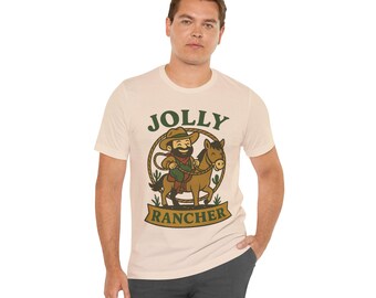 May include: Beige t-shirt with a cartoon cowboy riding a horse, encircled by a rope design. The text "JOLLY RANCHER" is printed above and below the illustration in green and brown.