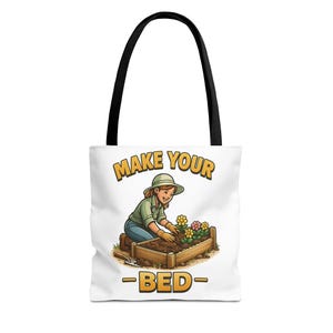 May include: White tote bag with black handles featuring a cartoon illustration of a person gardening. The text "MAKE YOUR BED" is displayed in yellow and brown. The illustration shows a person planting flowers in a wooden planter box.