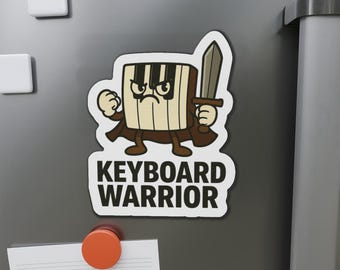 May include: A cartoon magnet featuring a keyboard character with a sword, brown cape, and angry expression. The text "KEYBOARD WARRIOR" is below the character. The magnet is on a gray surface with other magnets.