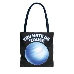 Puede incluir: Bolso tote negro con asas azul marino. La bolsa presenta el texto "YOU HATE US 'CAUSE" en blanco, arqueado sobre un gráfico de planeta azul. Un accesorio elegante y funcional.