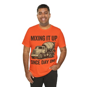 May include: Orange t-shirt with the text "MIXING IT UP SINCE DAY ONE" above and below a graphic of a cement mixer truck. The shirt is a crew neck style and is made of a soft material.