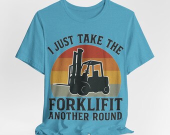 May include: A turquoise t-shirt featuring a black forklift silhouette set against a retro sunset design. The text reads "I JUST TAKE THE FORKLIFT ANOTHER ROUND" in a bold, vintage font. The shirt is made of a soft material.