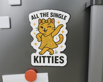 May include: A magnet with a cartoon cat in a gold sparkly dress, winking and dancing. The text reads "ALL THE SINGLE KITTIES" in a playful font, with star accents. The magnet is on a grey surface.