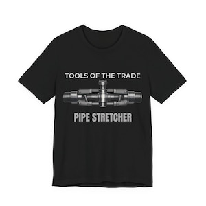 Puede incluir: Camiseta negra con el texto "TOOLS OF THE TRADE" sobre una ilustración detallada de un estirador de tuberías. El texto "PIPE STRETCHER" está debajo en una fuente en negrita sin serifa. El diseño está centrado en la camiseta.