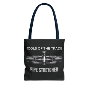May include: Black tote bag with navy blue handles. The bag features the text "TOOLS OF THE TRADE" above a silver pipe stretcher graphic, with "PIPE STRETCHER" printed below. The bag is designed for carrying items.
