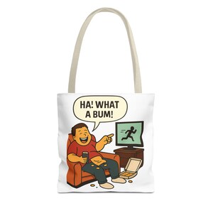 Puede incluir: Bolso tote blanco con una ilustración de dibujos animados de una persona riendo mientras ve la televisión. La persona está sentada en una silla naranja, sosteniendo una lata y tiene comida en su regazo. El texto "HA! WHAT A BUM!" está en un bocadillo.