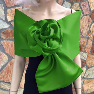 May include: A vivid green satin shawl featuring a large, sculpted rose. The shawl is draped over the shoulders, creating a dramatic and elegant look. The bright colour and floral accent make it a statement piece for special occasions.