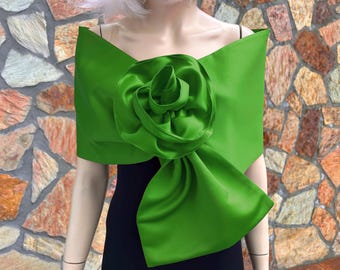 Könnte beinhalten: Ein leuchtend grüner Satin-Schal mit einem großen, geformten Rosendetail. Der Schal wird über die Schultern drapiert und erzeugt einen dramatischen und eleganten Look. Die leuchtende Farbe und der florale Akzent machen ihn zu einem Statement-Stück für besondere Anlässe.