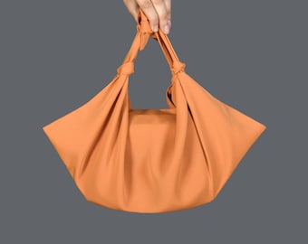May include: A bright orange fabric tote bag with a knotted handle. The bag is made of a soft, pliable material and is folded flat.