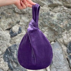 May include: A purple velvet bag with a knotted handle. The bag is small and round, and the handle is long enough to be carried over the shoulder.