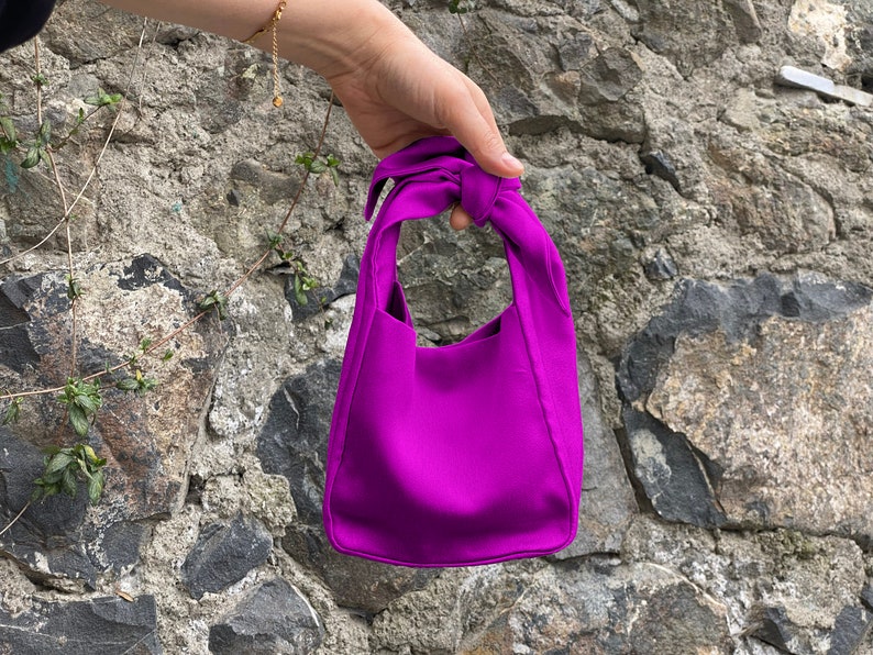 May include: A small, bright purple handbag with a knotted handle.