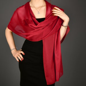 May include: A red sheer scarf draped over a black dress. The scarf is worn as a shawl and is tied at the neck.