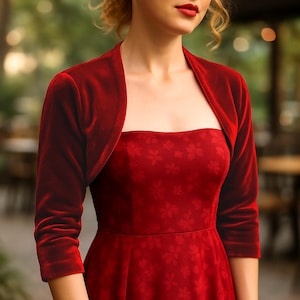 Puede incluir: Un bolero de terciopelo rojo intenso con mangas tres cuartos. Se lleva sobre un vestido rojo a juego con un estampado floral. El conjunto crea un look cohesivo y elegante, adecuado para eventos formales u ocasiones especiales.