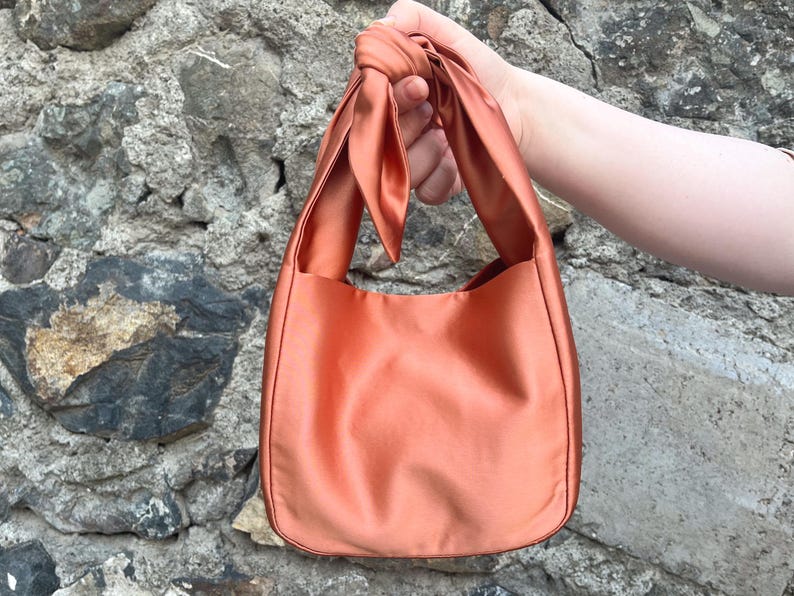 May include: A small, terracotta-coloured, satin tote bag with a knotted handle.