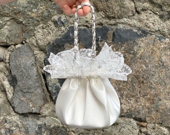 Pode incluir: Uma bolsa de cordão de cetim branco com uma alça de corrente prateada e uma borda de renda branca.