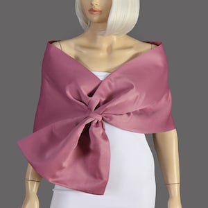 May include: A mauve satin shawl with a large bow in the front. The shawl is draped over a white dress form.