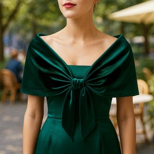 Puede incluir: Vestido verde esmeralda oscuro con detalle de lazo de terciopelo a juego. El lazo está centrado en el pecho y tiene un diseño drapeado con hombros descubiertos. El vestido tiene un escote cuadrado y un corpiño ajustado.