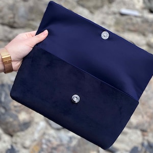 Op de afbeelding: Een donkerblauwe clutch van fluweel met een zilveren drukknoop.