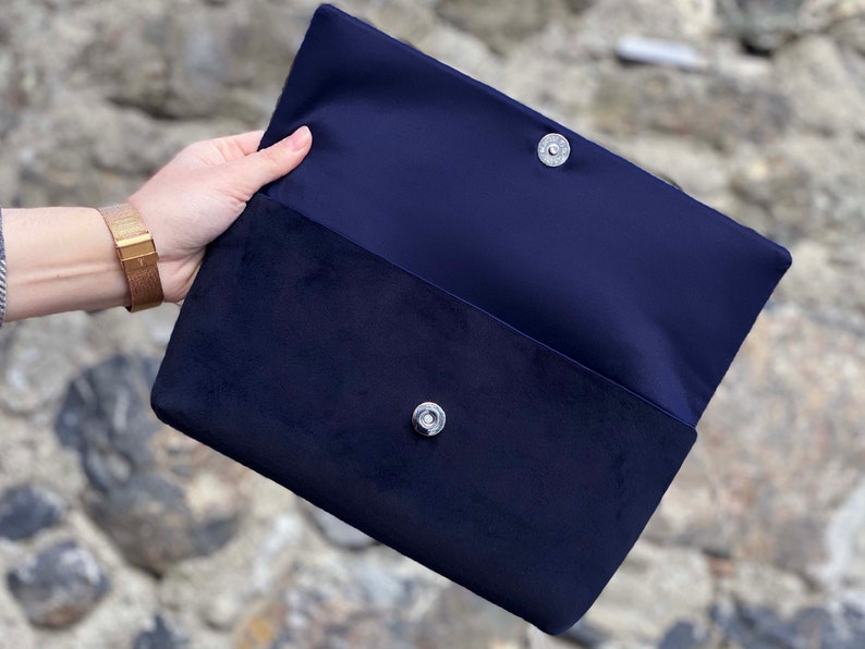 Op de afbeelding: Een donkerblauwe clutch van fluweel met een zilveren drukknoop.