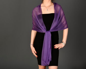Pode incluir: Um xale de chiffon roxo drapeado sobre um vestido preto. O xale está amarrado no pescoço e cai até a cintura.