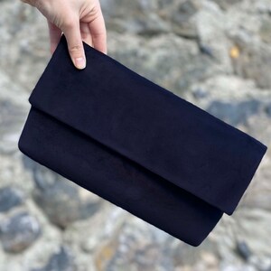 Op de afbeelding: Een donkerblauwe su&egrave;de clutch met een omslagklep.