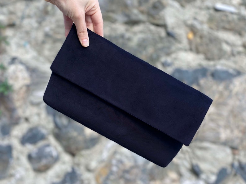 Op de afbeelding: Een donkerblauwe su&egrave;de clutch met een omslagklep.