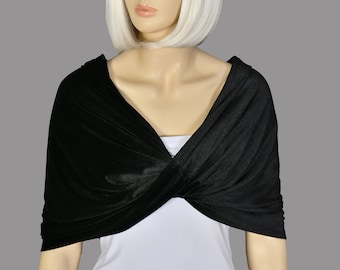May include: A solid black wrap shawl featuring a twisted front design that crosses over the chest. The fabric has a smooth, slightly reflective finish and is draped over a plain white top, creating a layered look with short sleeves.