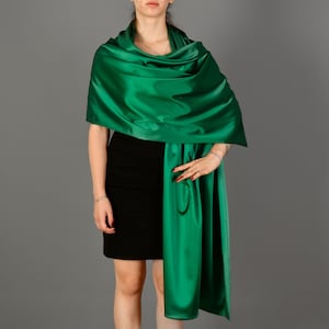 Può includere: Un scialle di raso verde drappeggiato sulle spalle di una persona. Lo scialle è annodato sul davanti e ha un'estremità lunga e fluida.