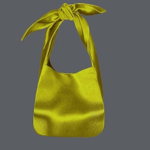 May include: A chartreuse-colored shoulder bag with a knotted handle. The bag has a soft, textured appearance and a rounded bottom. The background is a solid gray.